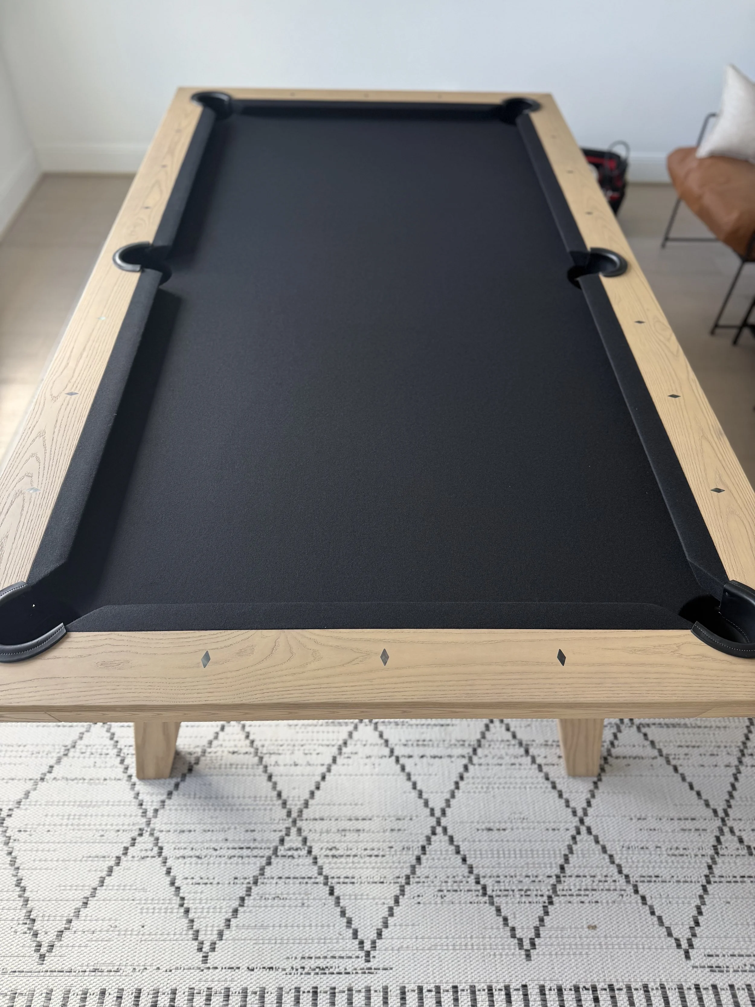 A rectangular air hockey table with a black playing surface and a natural wood frame, resting on a woven rug with a geometric black and white pattern.
