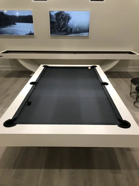 Indoor game room with a black pool table and a white frame, billiard balls on the table, and two wall-mounted screens showing nature scenes.