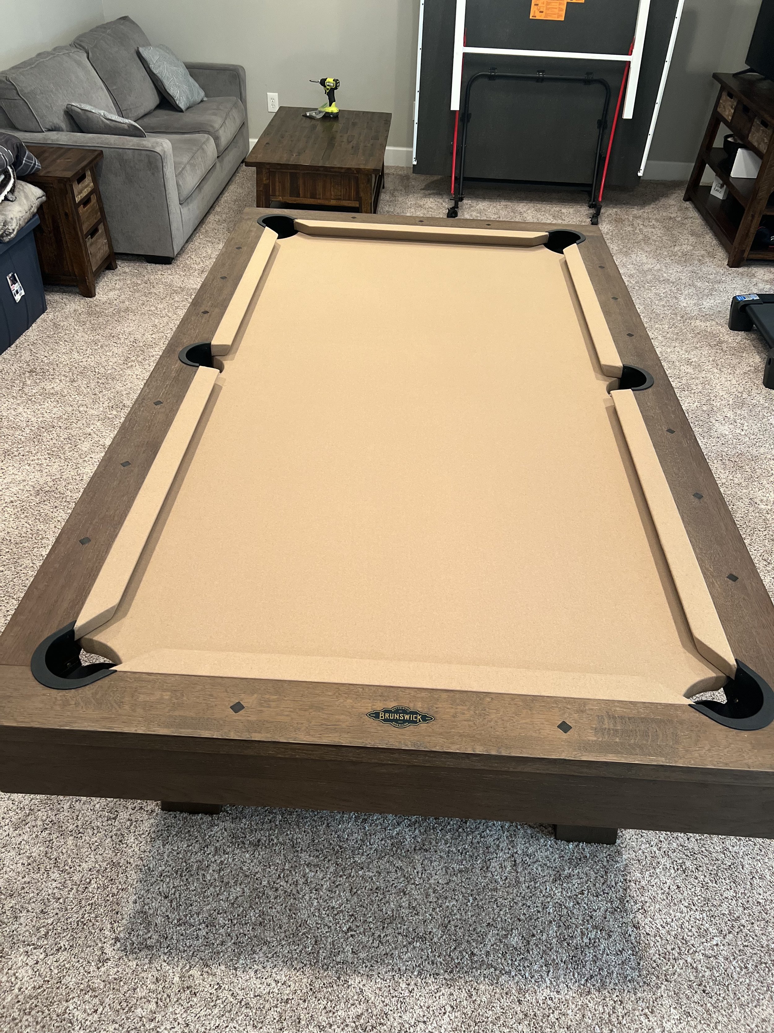 A Brunswick pool table on a carpeted floor with a label on the front.