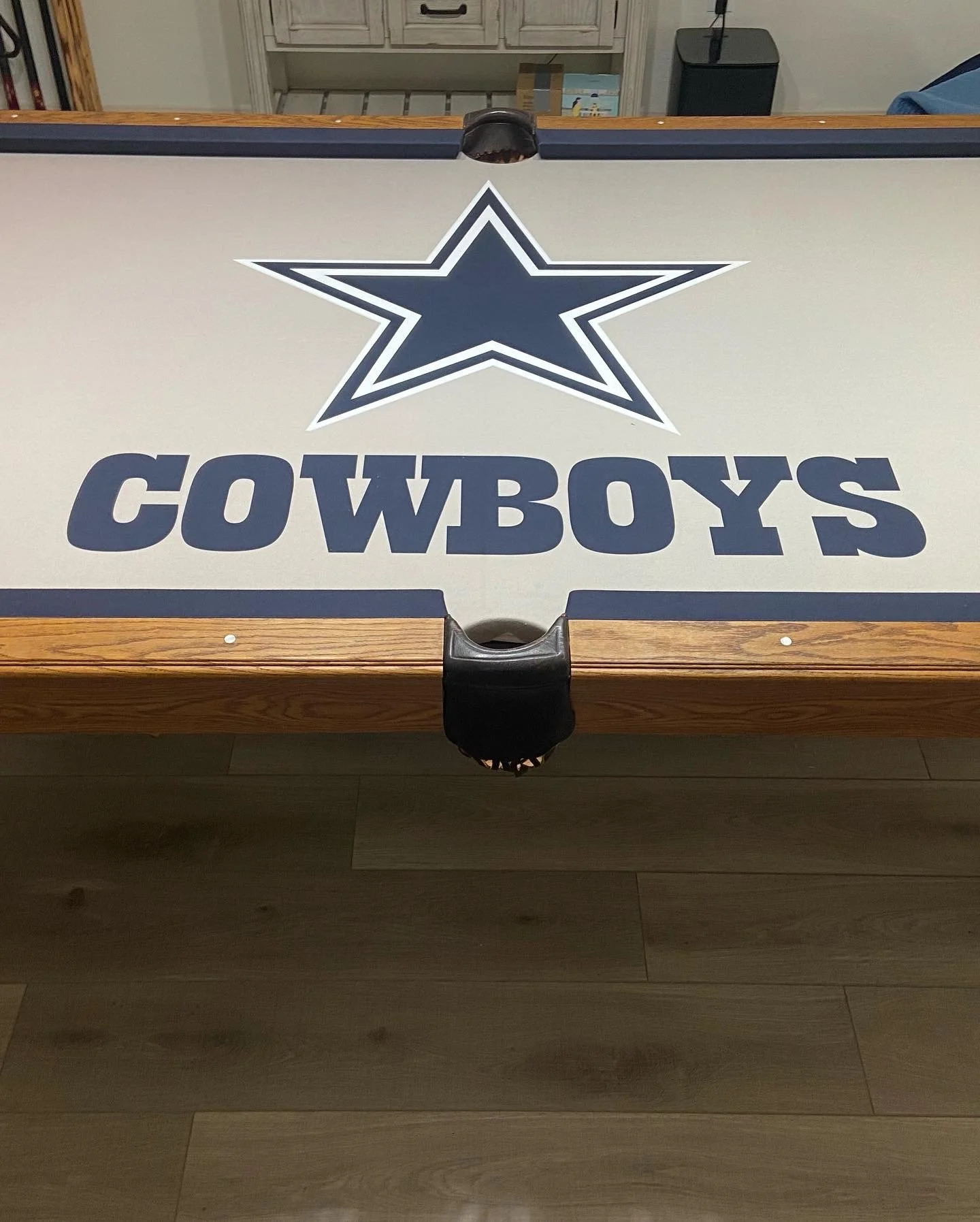 A foosball table with a Dallas Cowboys logo and text, seen upside down, situated in a room with wooden flooring and a cabinet in the background.