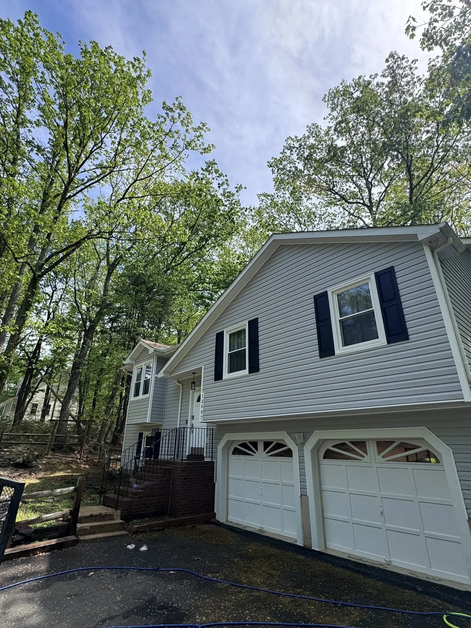 A white two-story house with black window shutters, a garage with a white door, thats beeen cleaned and pressure washed soft washed and power washed