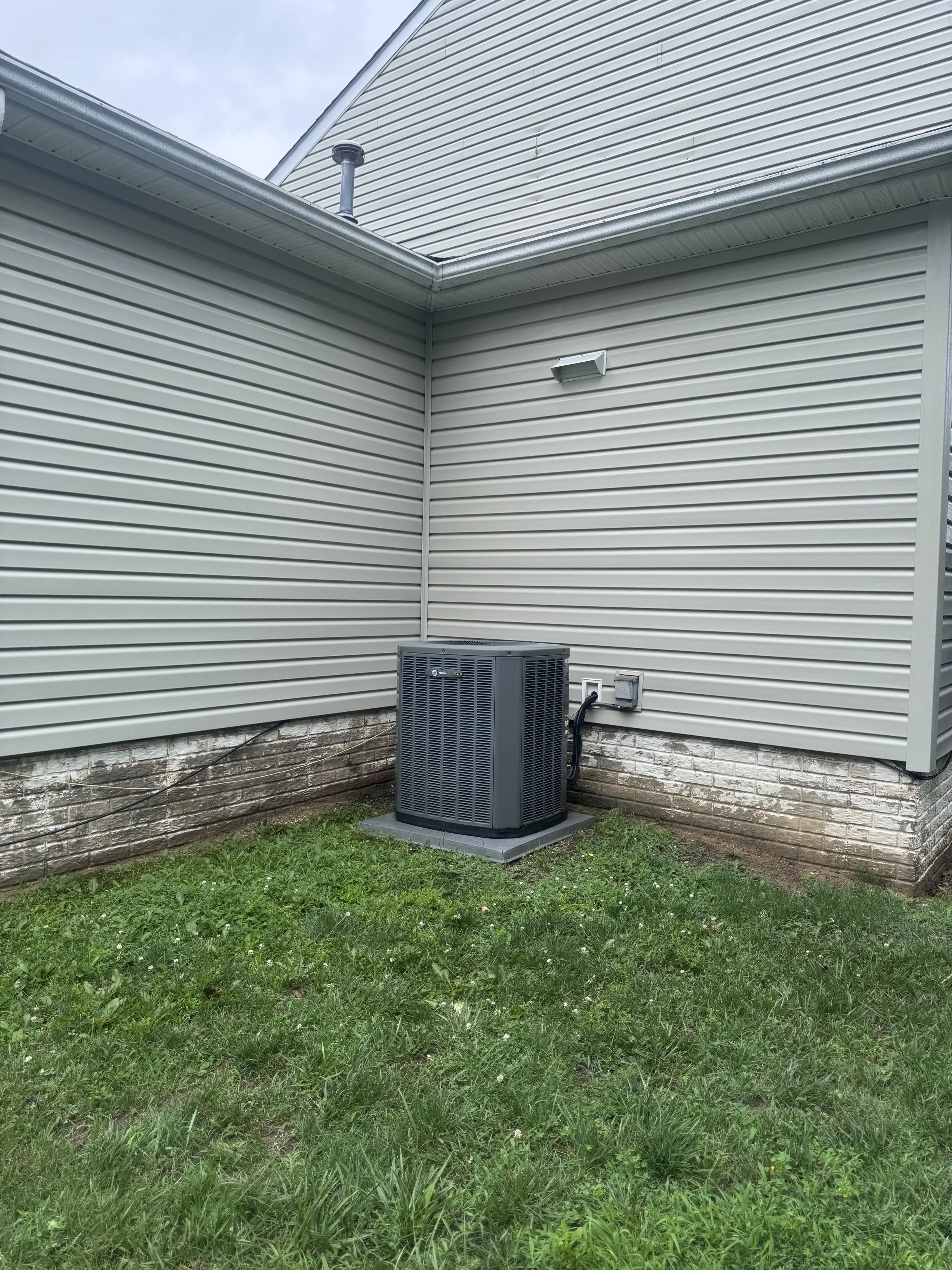 Backyard with grass, house siding, an air conditioning unit, and a vent on the wall.