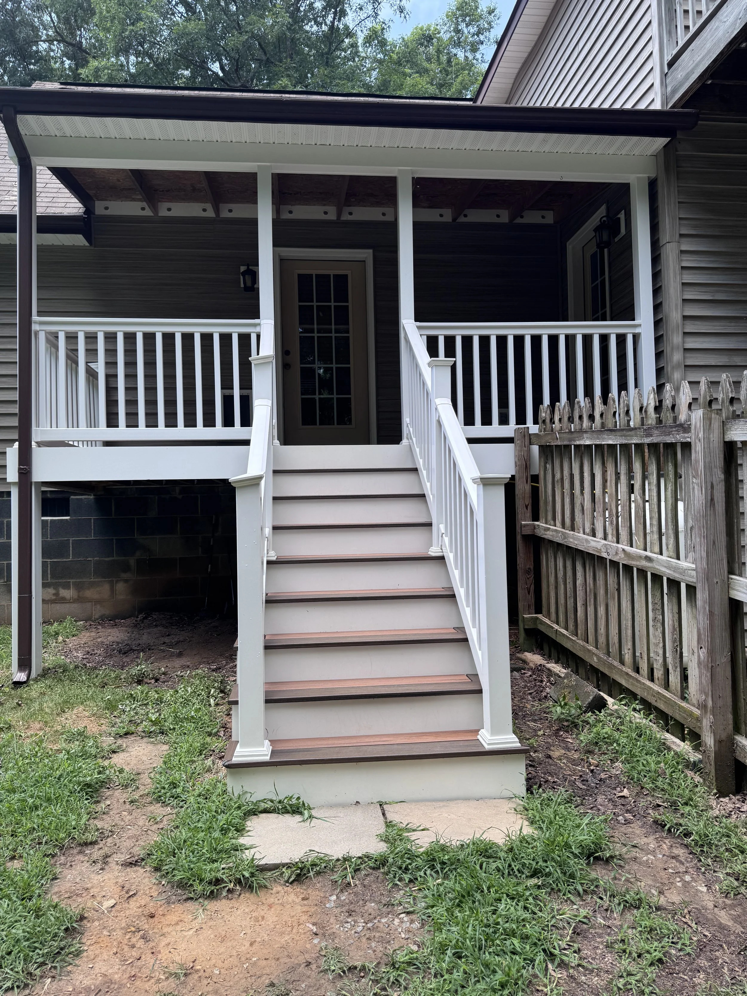 Backyard with a porch, stairs, a wooden fence, and a small patch of grass and dirt.