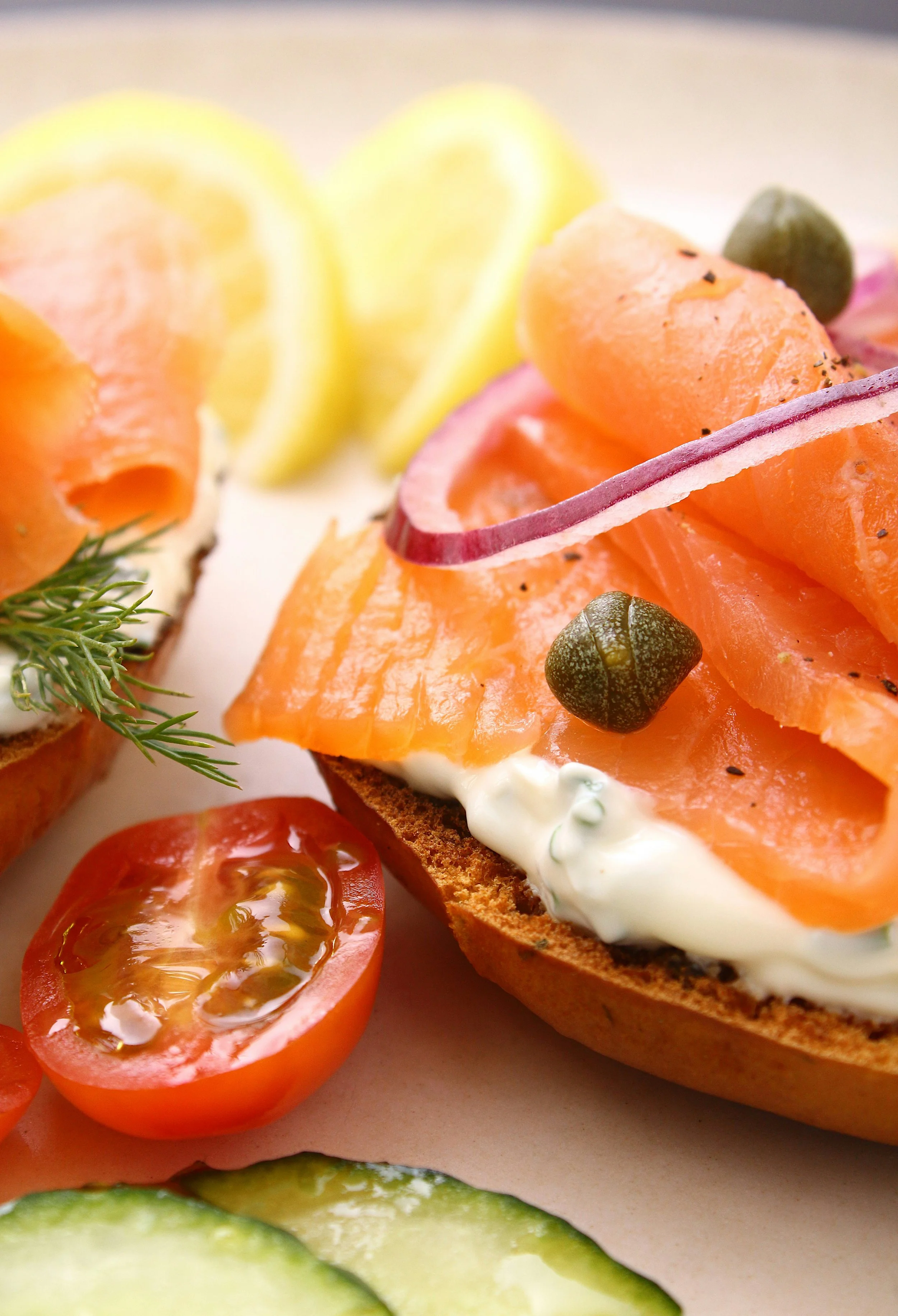 Close-up of open-faced smoked salmon sandwich with cherry tomatoes, cucumber slices, and lemon wedges