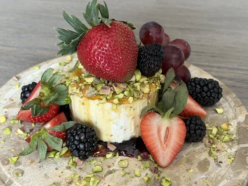 Cheesecake topped with strawberries, blackberries, red grapes, chopped pistachios, and drizzled with berry sauce, garnished with fresh fruit on a plate.