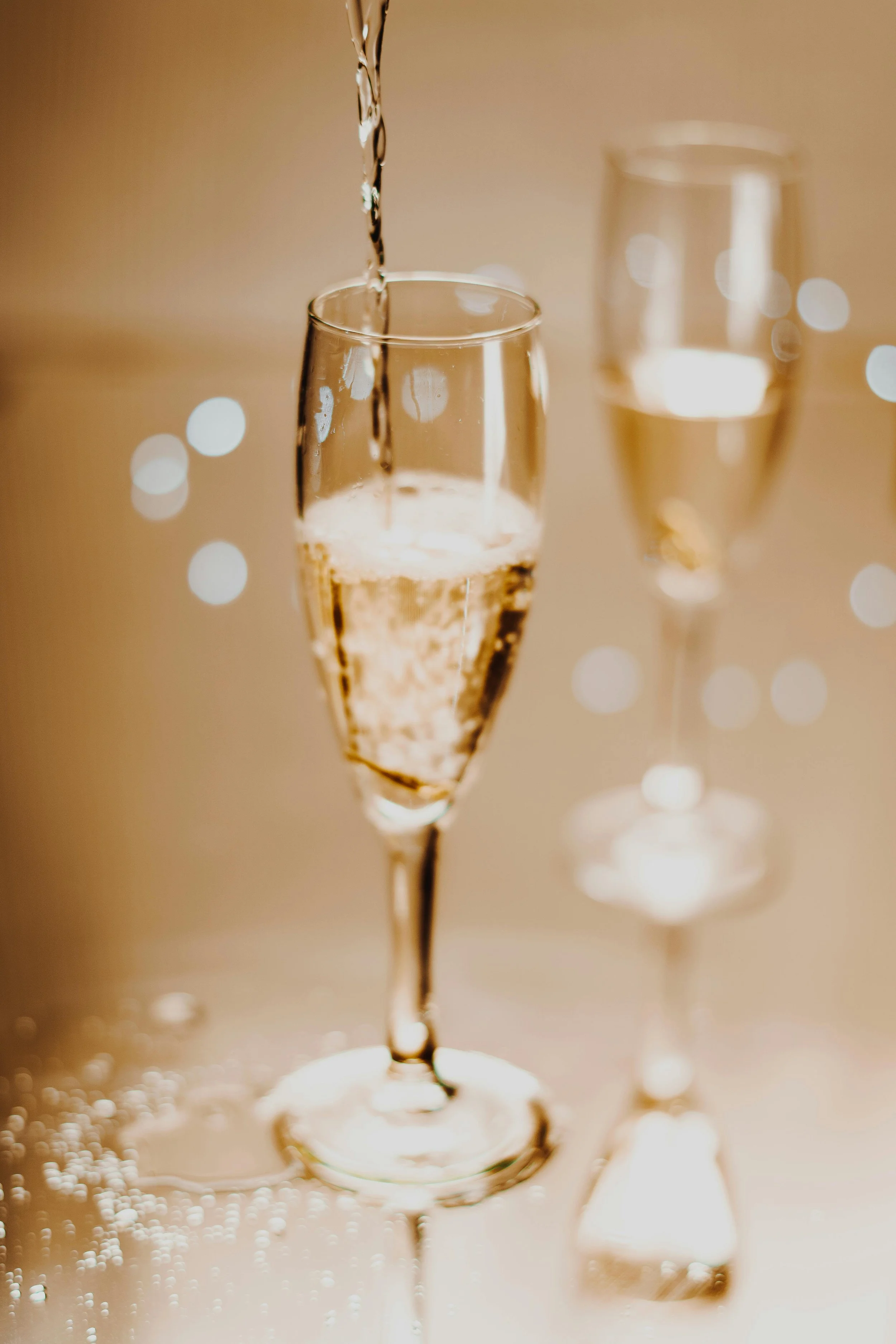 Champagne glasses and a bottle pouring champagne with a blurred background and bokeh lights.