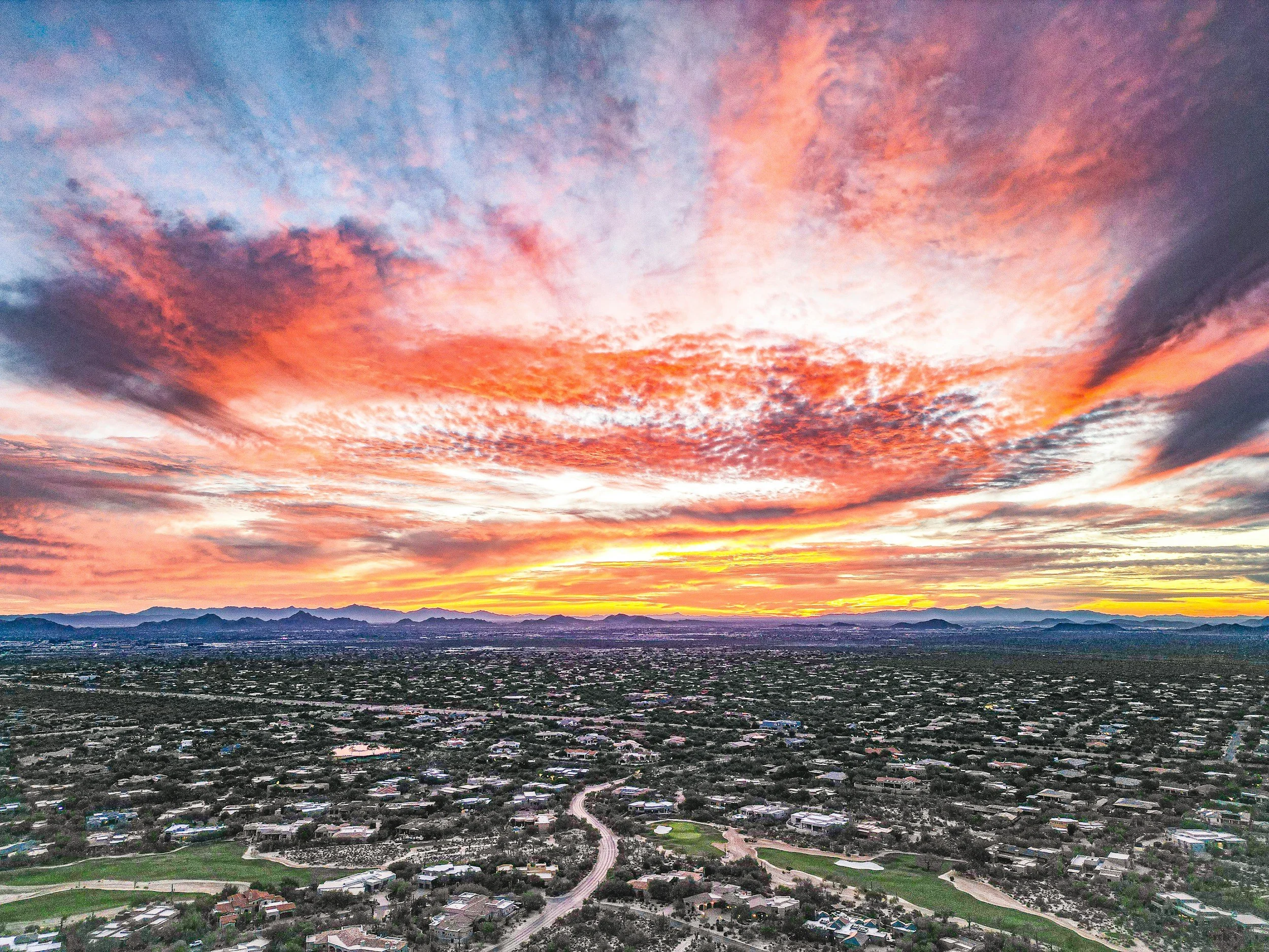 A colorful sunset over a sprawling city with mountains in the background.