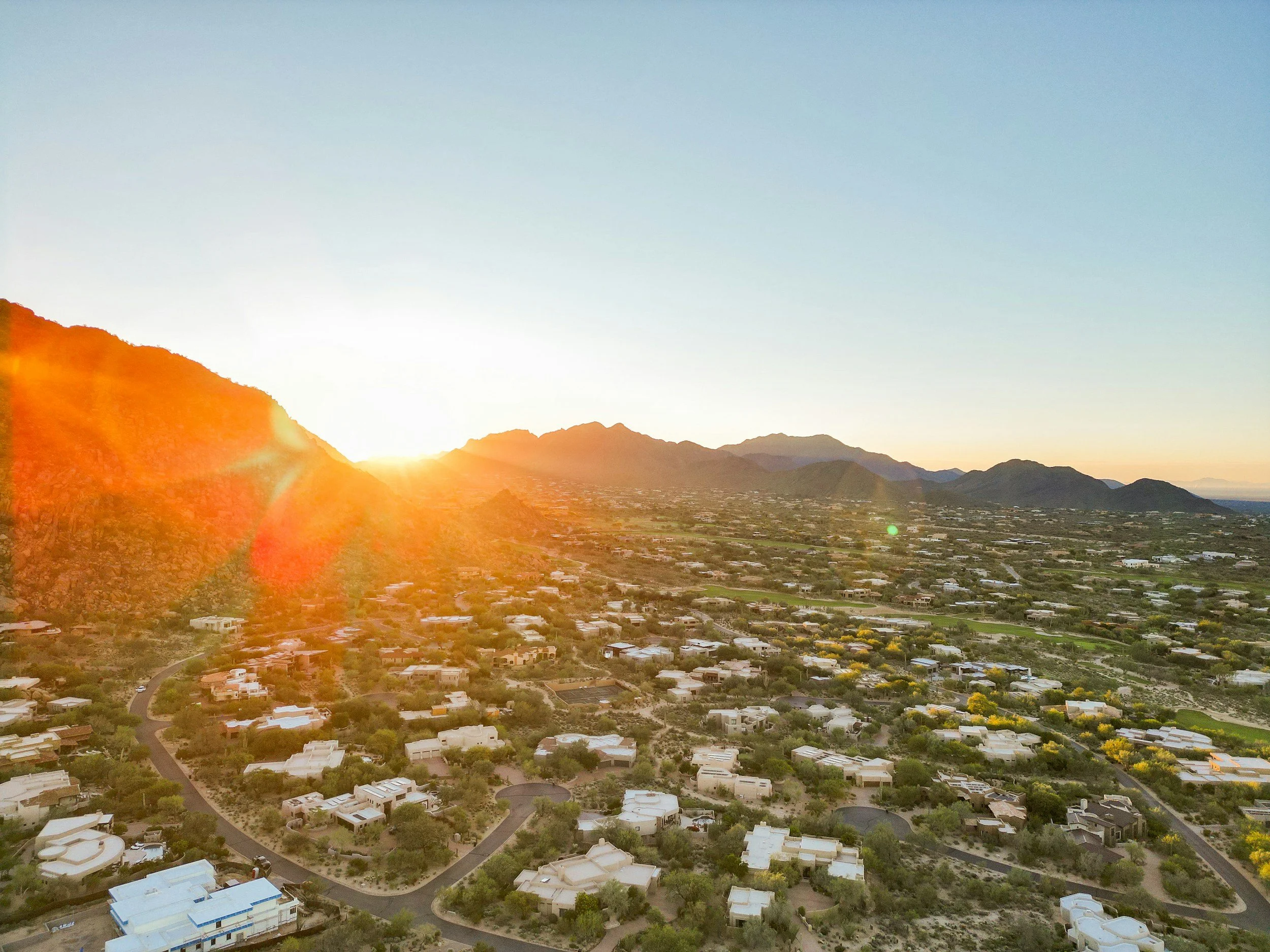 Aerial view of a suburban neighborhood at sunset with mountains in the background and a clear sky.
