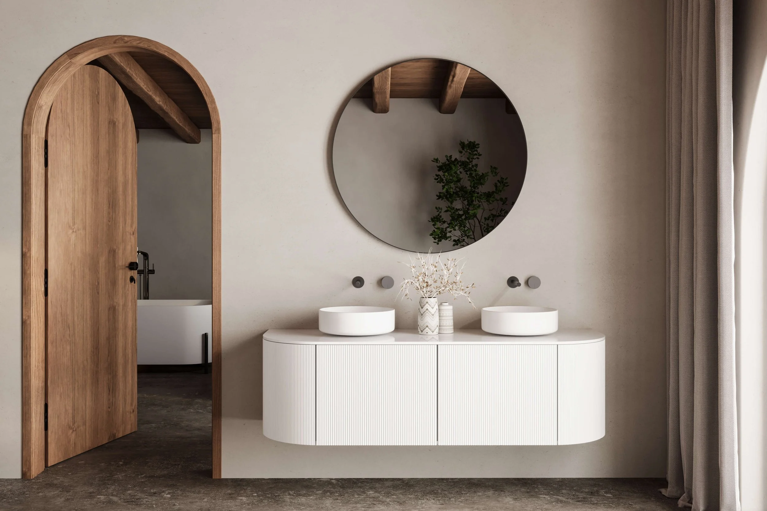 Modern bathroom with arched doorway. White mounted vanity cabinet with raised sinks. Round mirror with gold accent. Light oak door opens to white freestanding tub with freestanding water faucet.