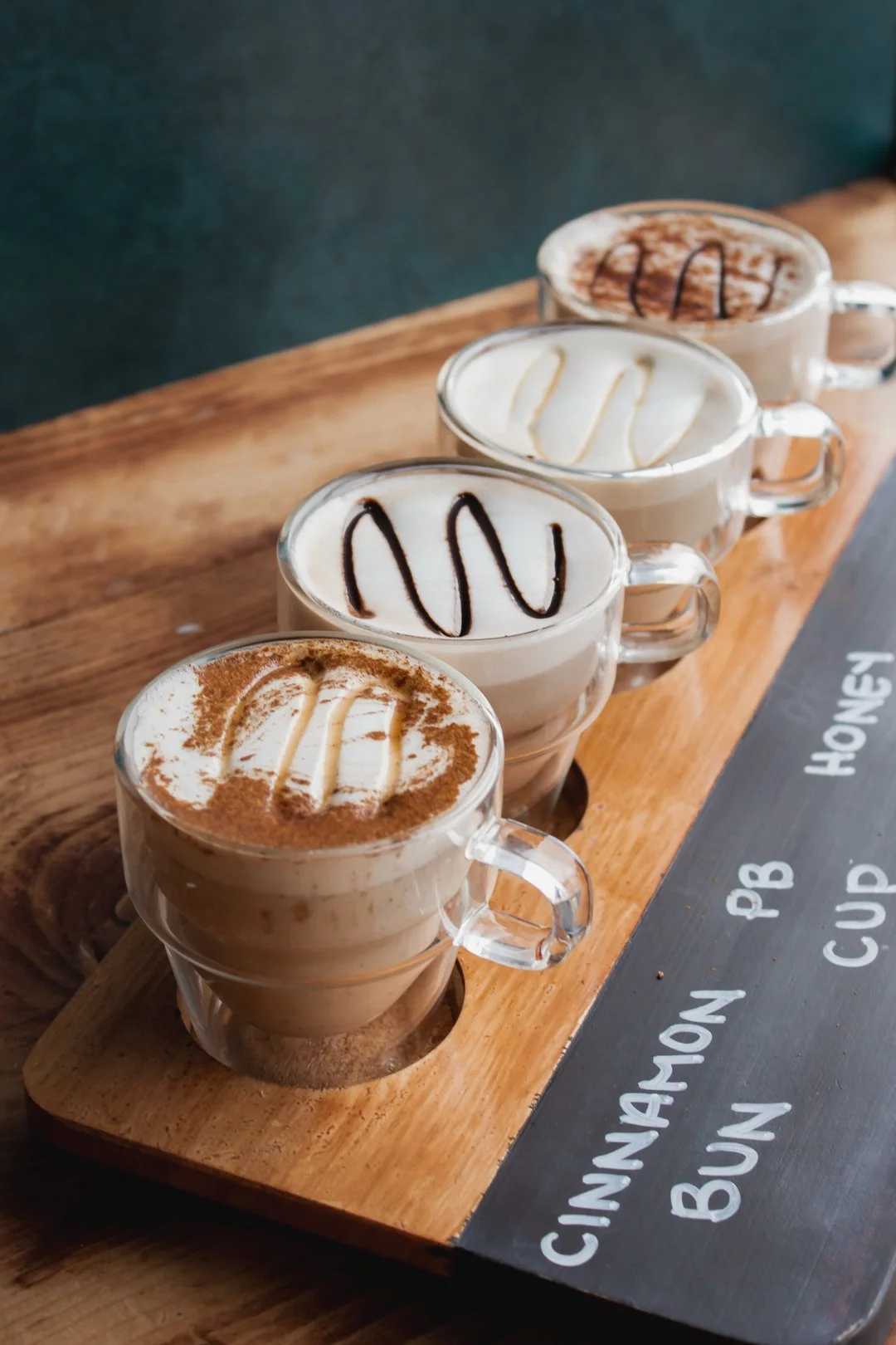 Four cups of coffee with different toppings on a wooden tray, lined up in a row.