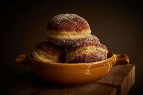 Four sugar-coated donuts in a brown ceramic bowl.