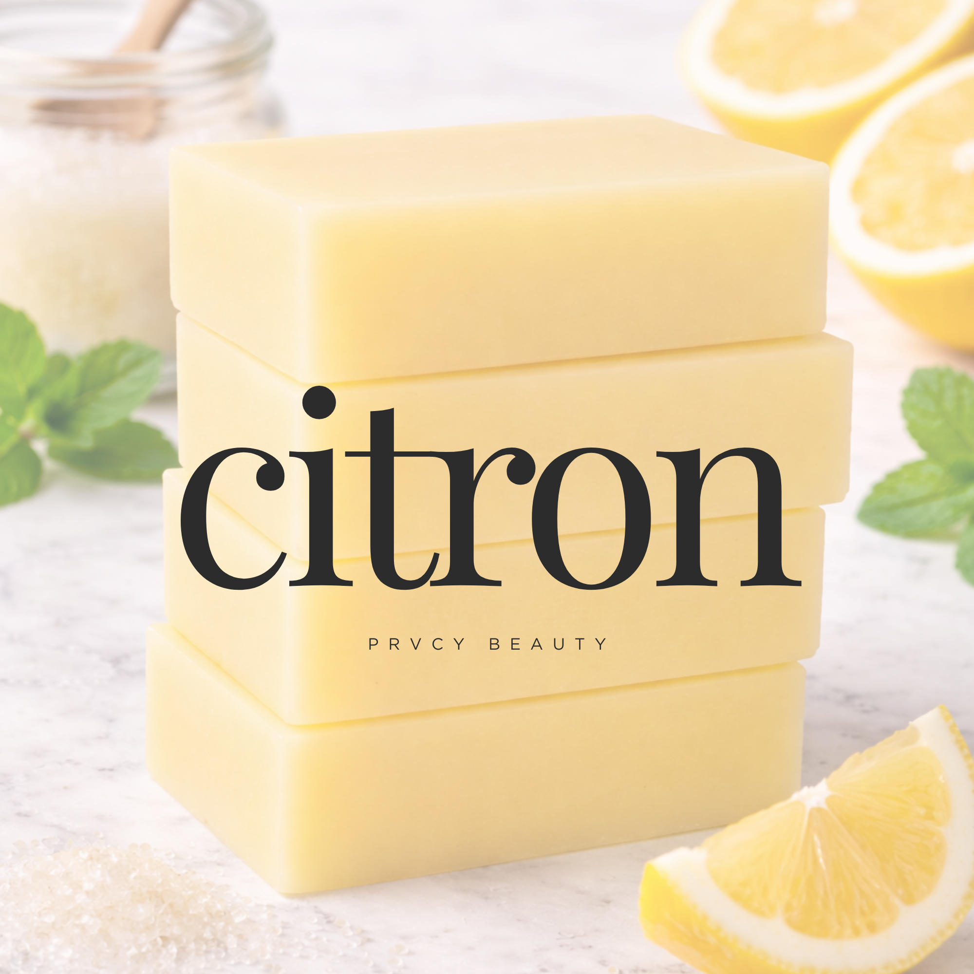 Stacked lemon-colored soap bars with lemon slices, mint leaves, and salt in the background on a white surface.