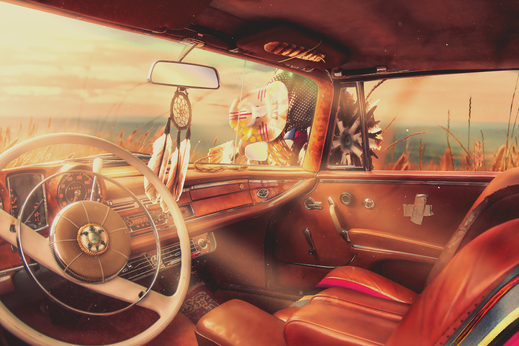 The interior of a vintage car with a brown dashboard and leather seats, set against a sunset landscape with wheat fields and dreamcatchers hanging inside the car.
