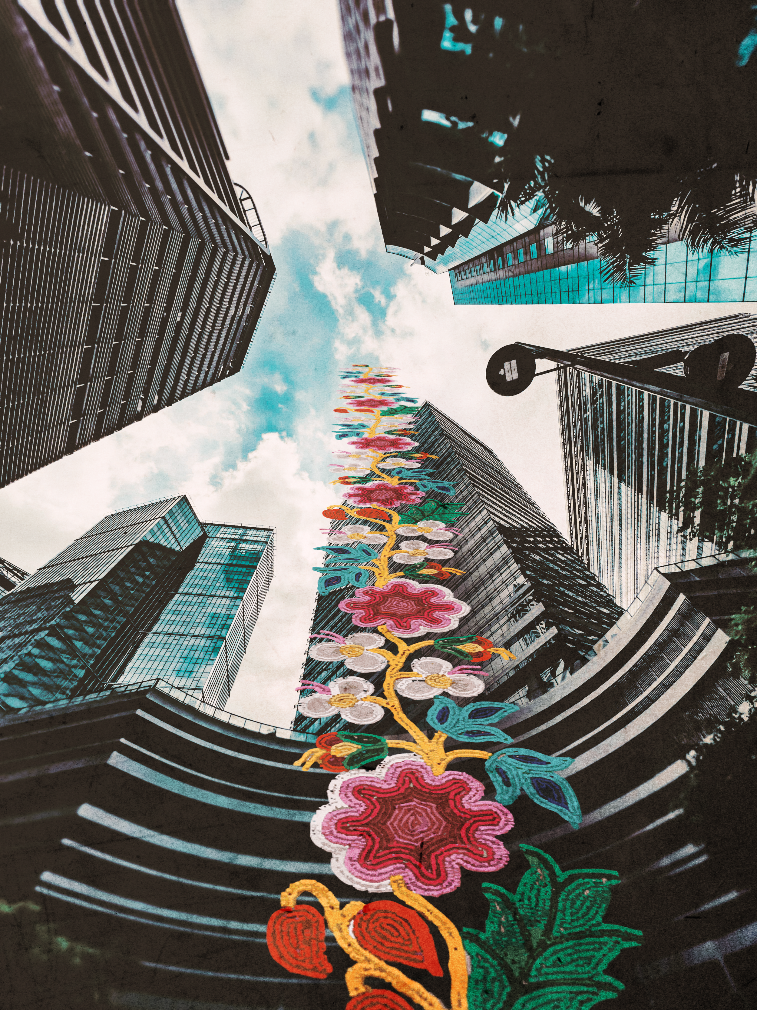 Colorful floral installation stretching between tall city buildings with glass facades, viewed from below upward towards the sky.