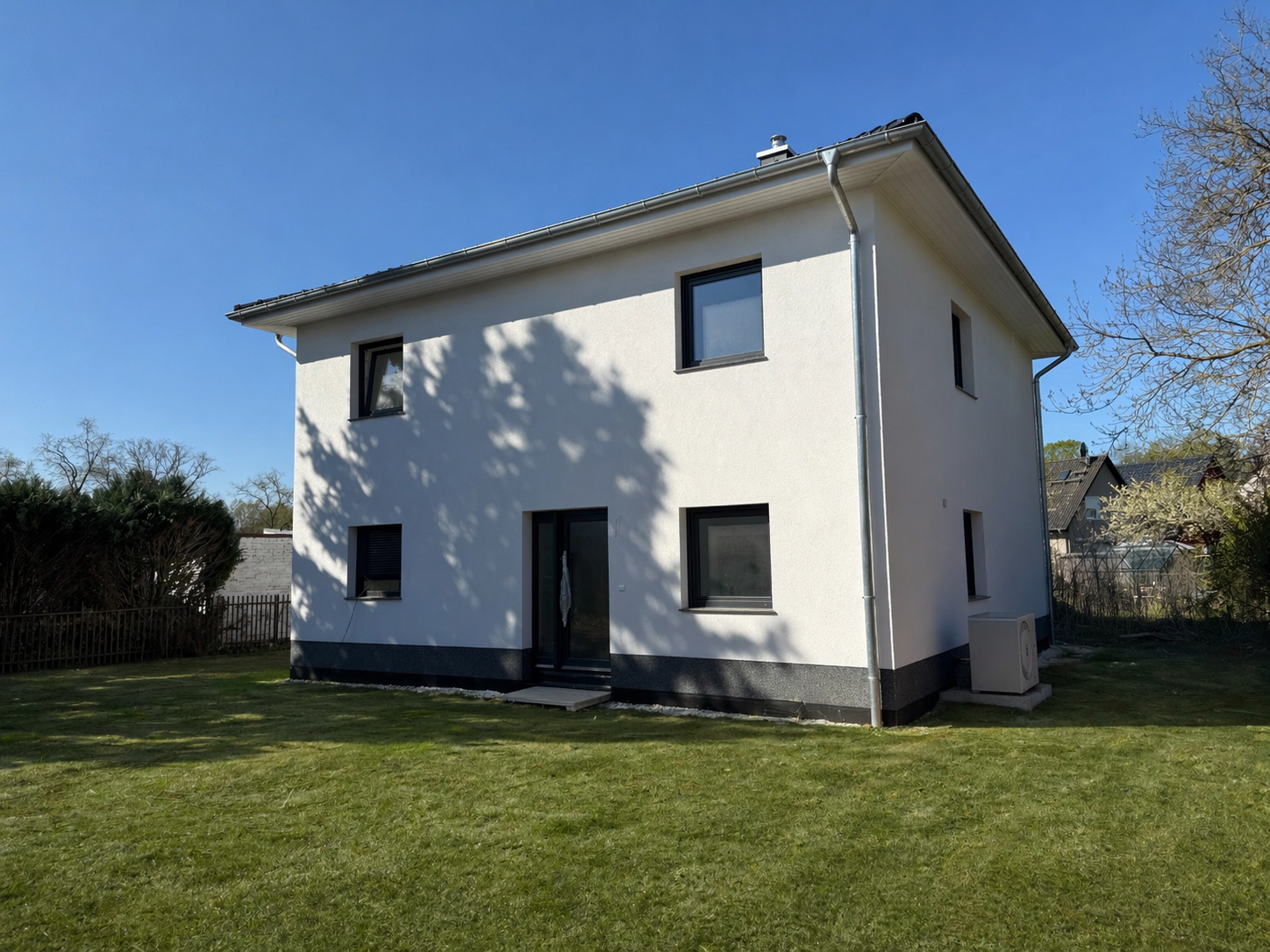 Ein modernes, weißes Einfamilienhaus mit schwarzem Dach, gelegen in einem Garten mit grünem Rasen und Bäumen.
