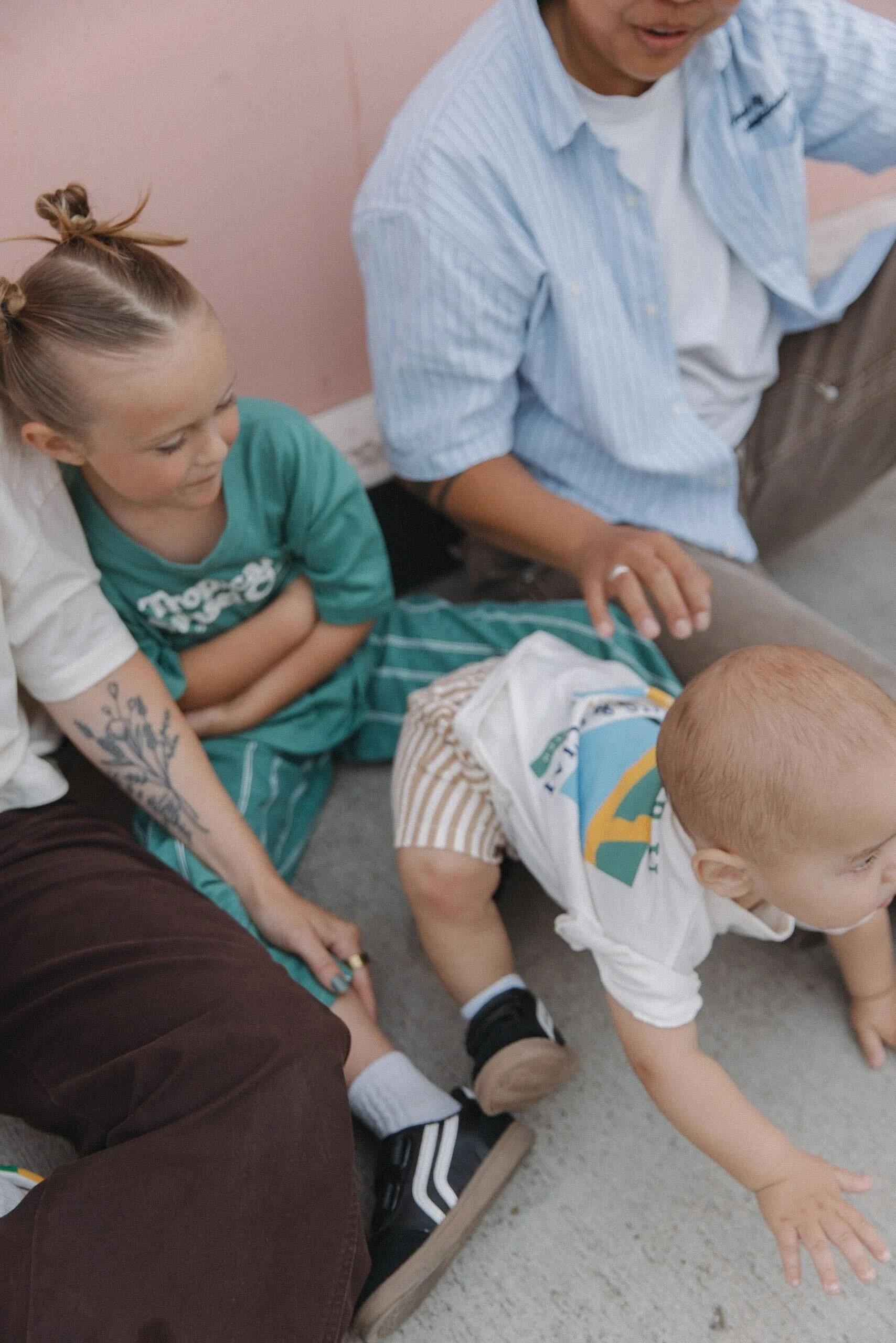 A young child with blonde hair crawling on the floor, surrounded by three adults and a young girl sitting nearby, all watching the child.