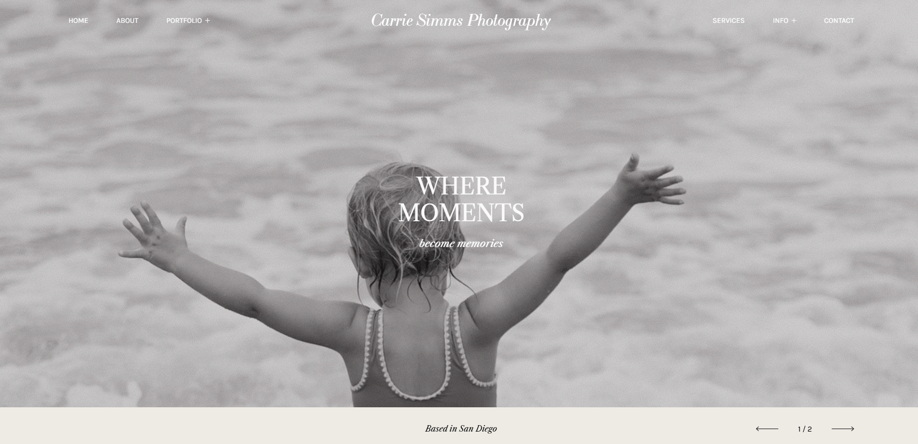 A black and white photo of a young girl at the beach with arms outstretched, facing away from the camera, with water in the background.