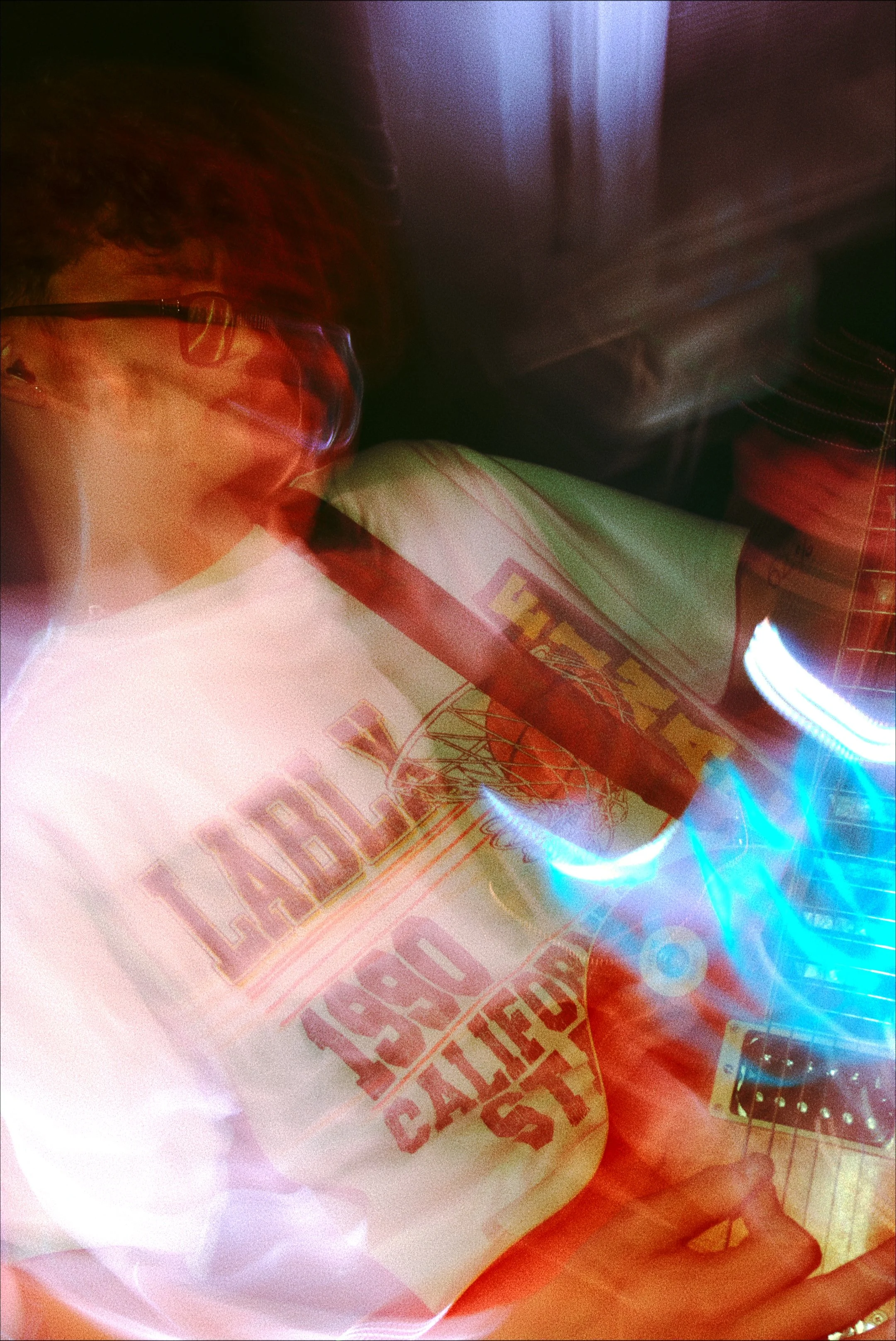 A person wearing glasses is holding a white bag with red and yellow text. The scene appears to have a light display with blue and red lights, creating a colorful, blurry effect.
