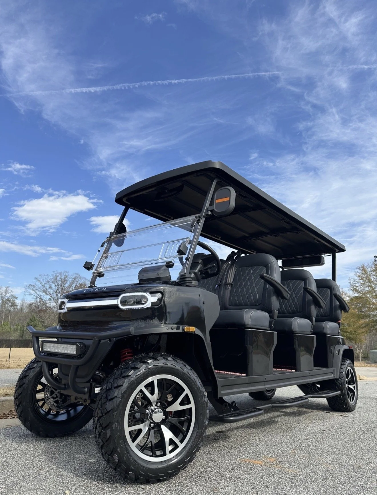 Black electric golf cart with four seats, large off-road tires, and a roof, parked outdoors under a blue sky with clouds.