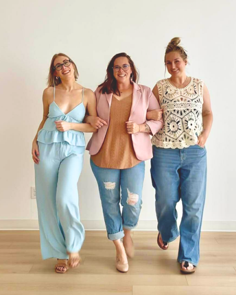 Three women walking together, smiling, indoors in front of a plain white wall.