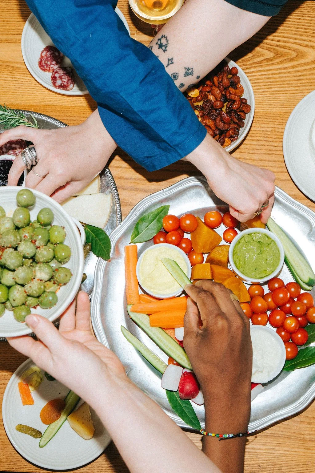 People sharing a colorful platter of fresh vegetables, cherry tomatoes, and dips during a meal.