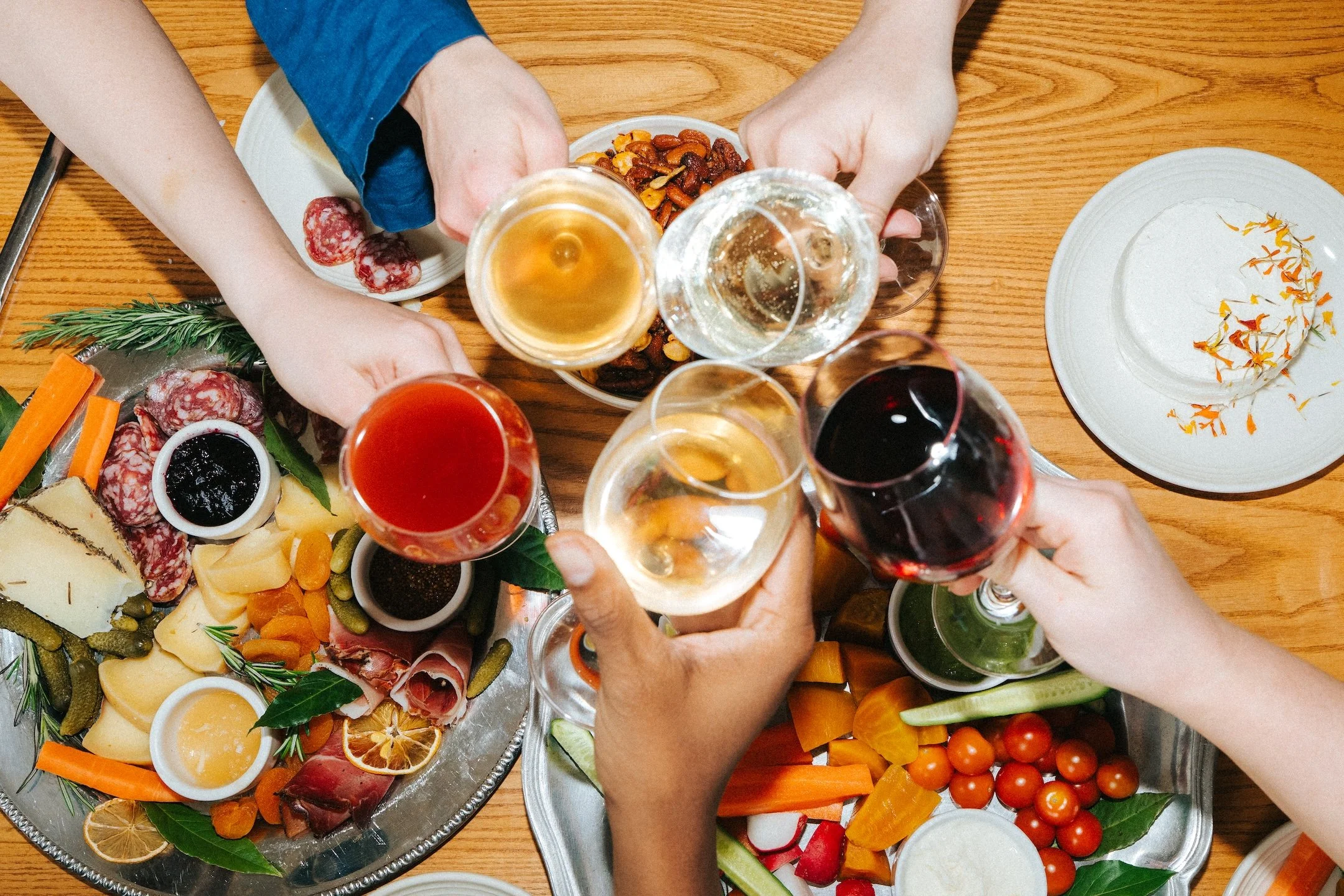 People raising glasses over an All Together Now cheese and charcuterie spread at a gathering.