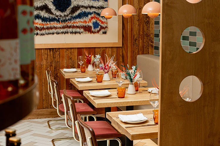 An intimate restaurant dining room with light wood tables, and colorful floral arrangements.