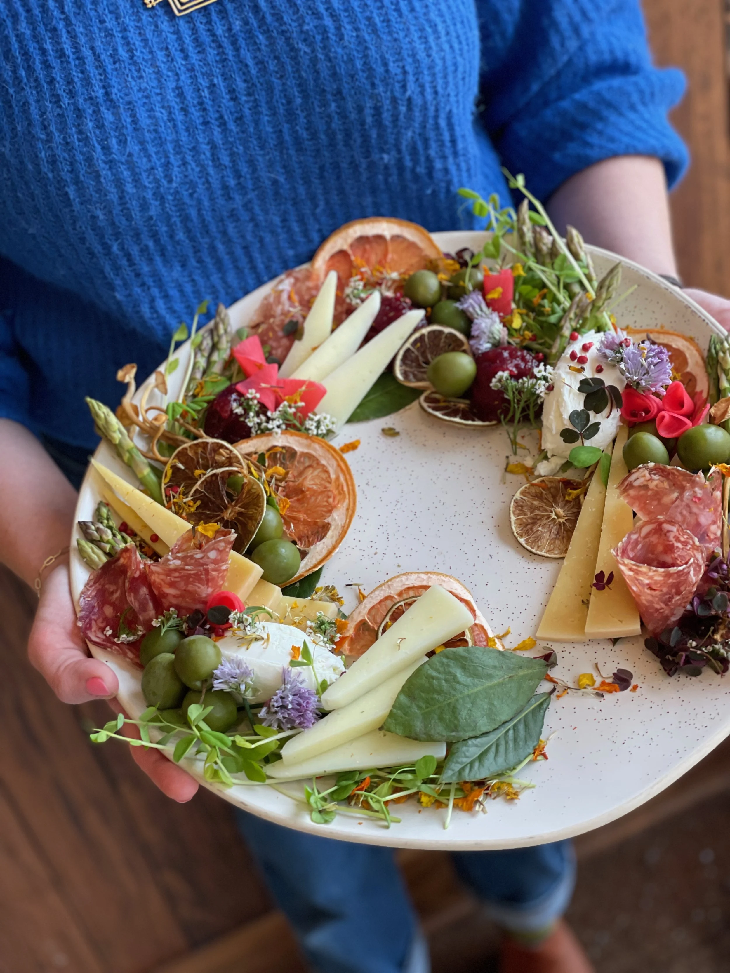 A person in a blue sweater holding a cheese and charcuterie board at a hands-on cheese workshop at All Together Now in Ukranian Village, Chicago.