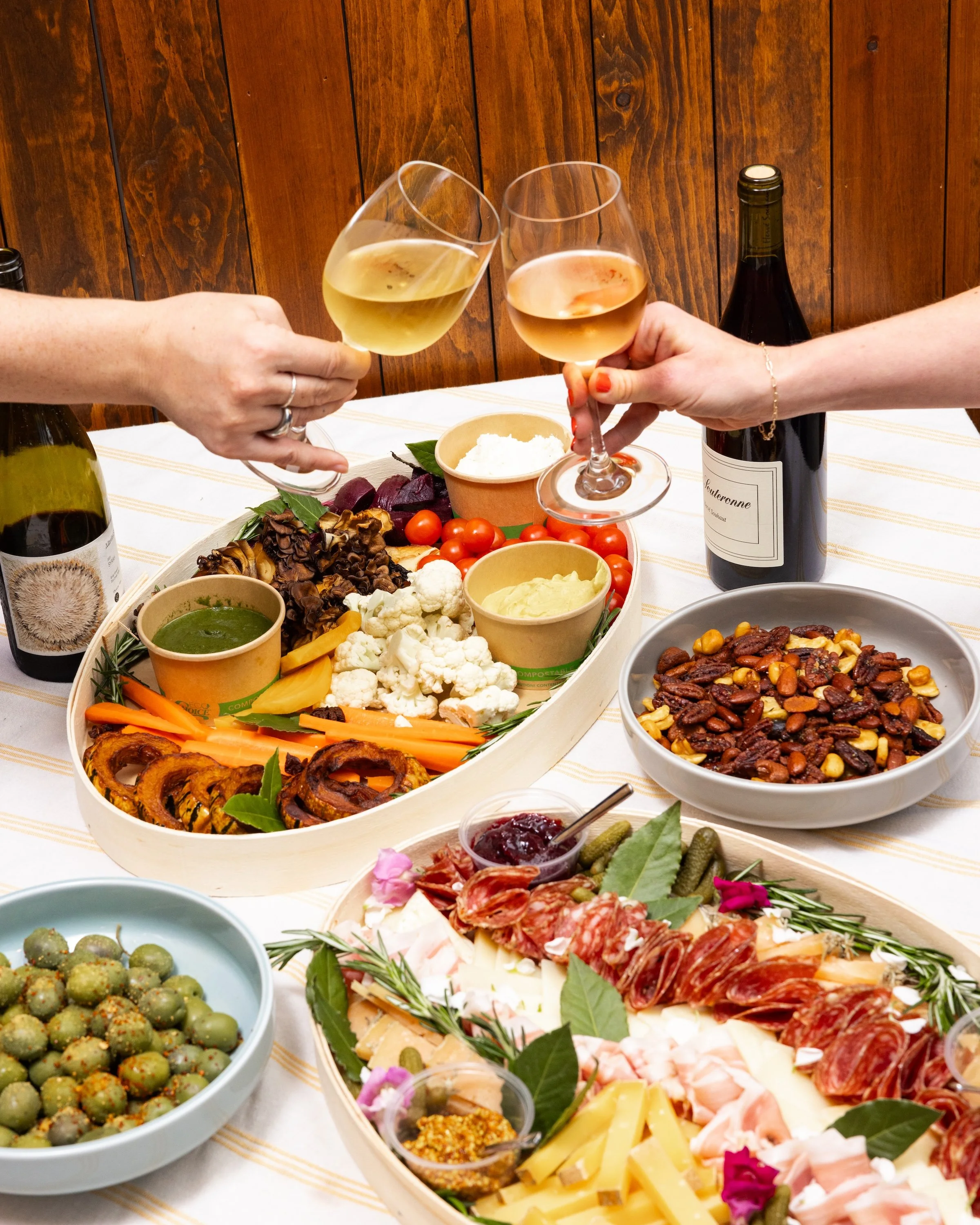 Guests raising wine glasses over an All Together Now cheese and charcuterie spread.