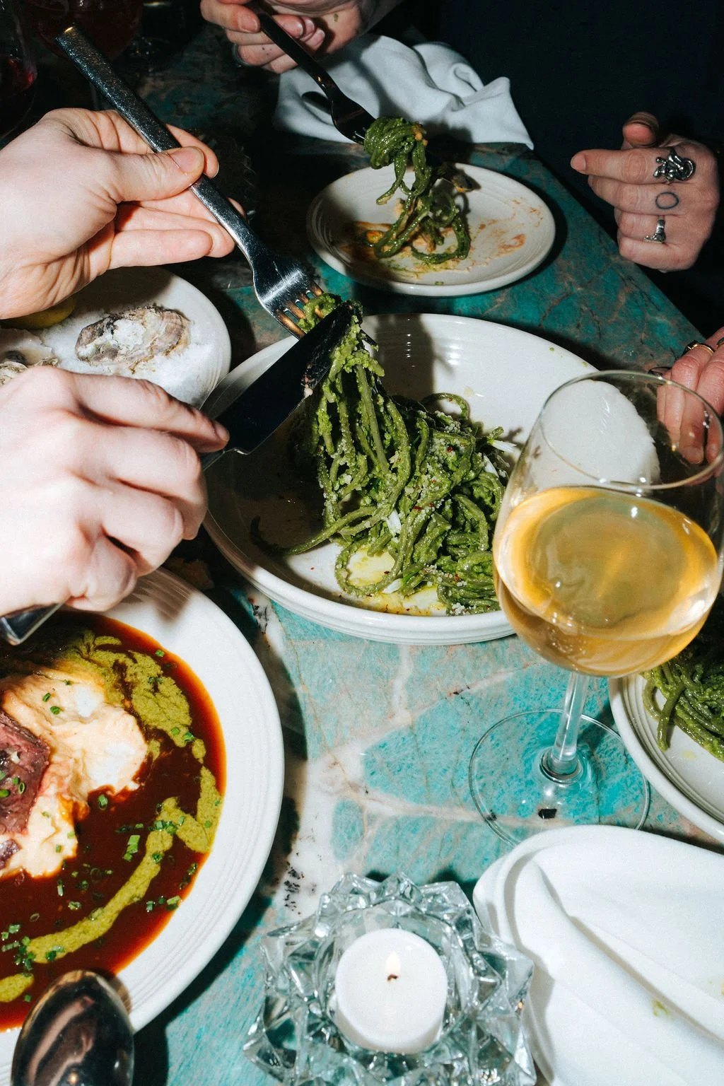 People sharing a Plate of Green Beans at a Dinner Table with Wine and Other Dishes