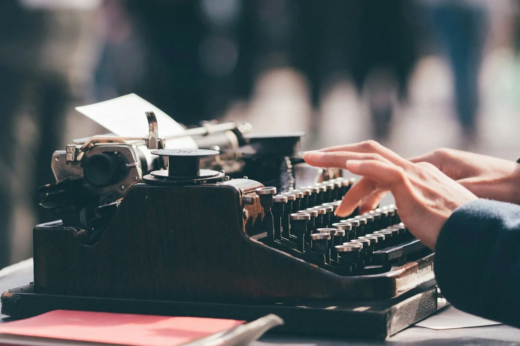 Close-up of a person's hands typing on a vintage typewriter with a blurred background.
