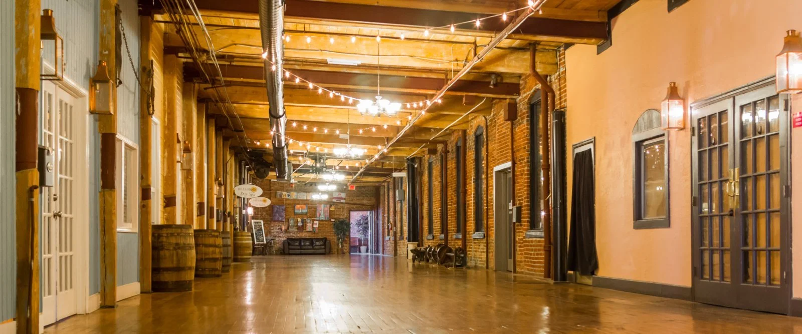 Empty hallway with wooden floors, exposed brick walls, string lights, and glass windows and doors.