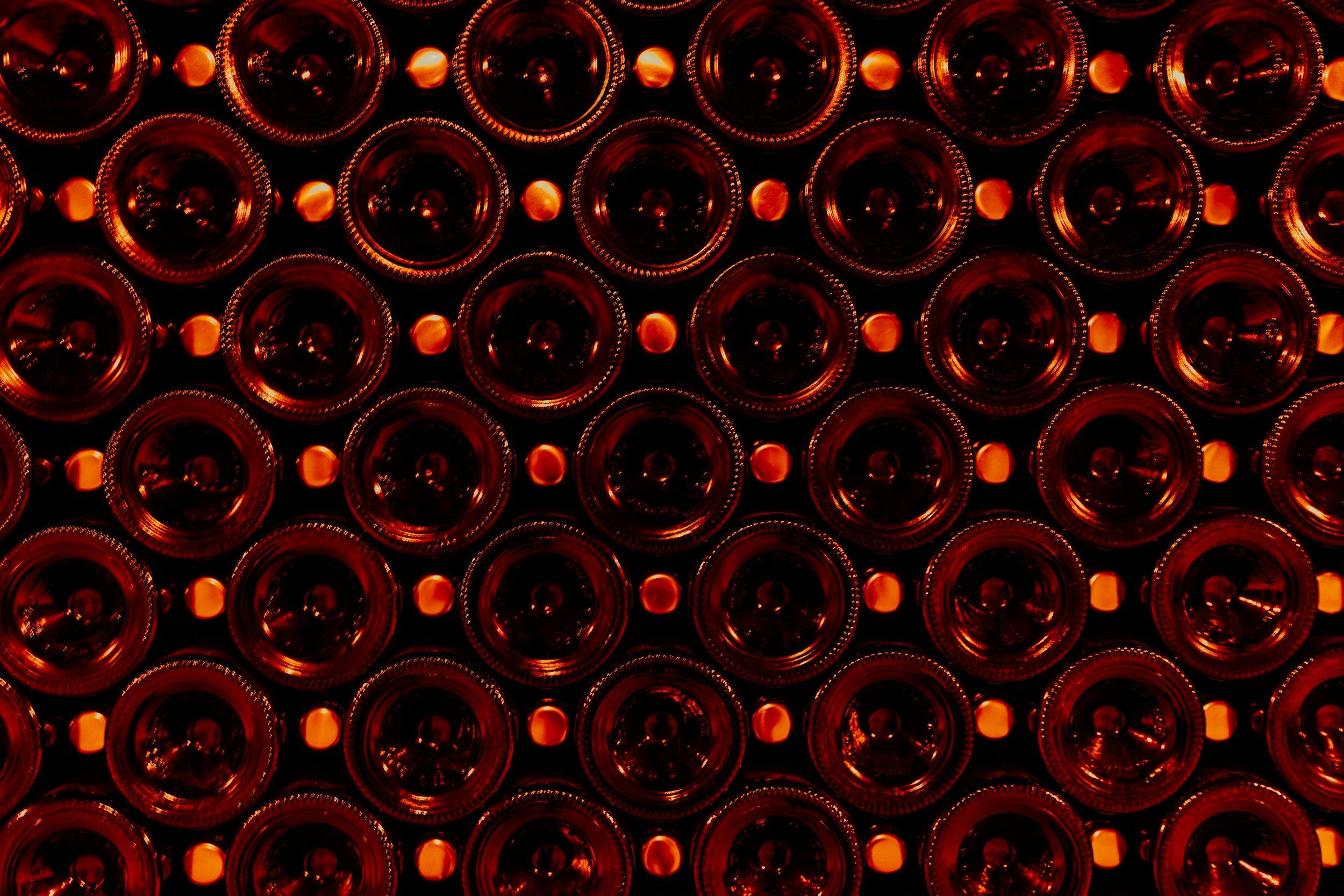 Multiple rows of upside-down bottles with orange caps, seen from below, illuminated with warm orange lighting.