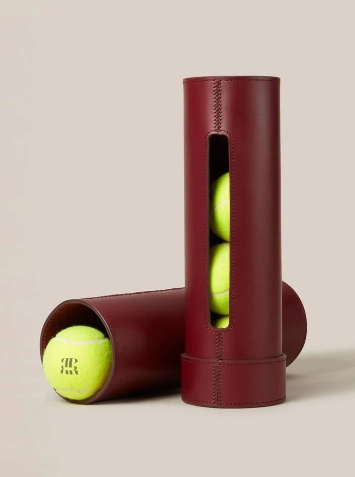 Two tennis balls stored in cylindrical leather cases, one case standing upright and the other lying on its side.