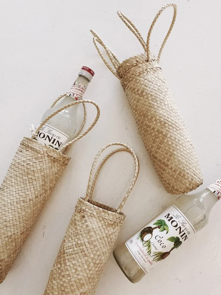Three woven straw bottle holders and two glass bottles of coconut drink on a white surface.