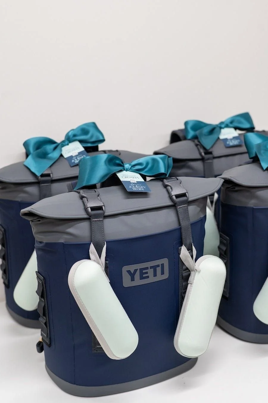 Multiple blue and gray YETI coolers with teal ribbons and tags placed on a white surface against a white background.