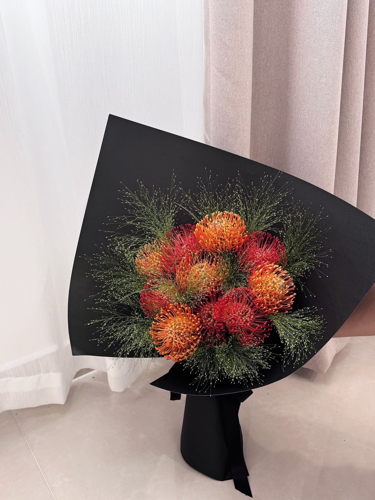 Bouquet of orange and pink exotic flowers wrapped in black paper.