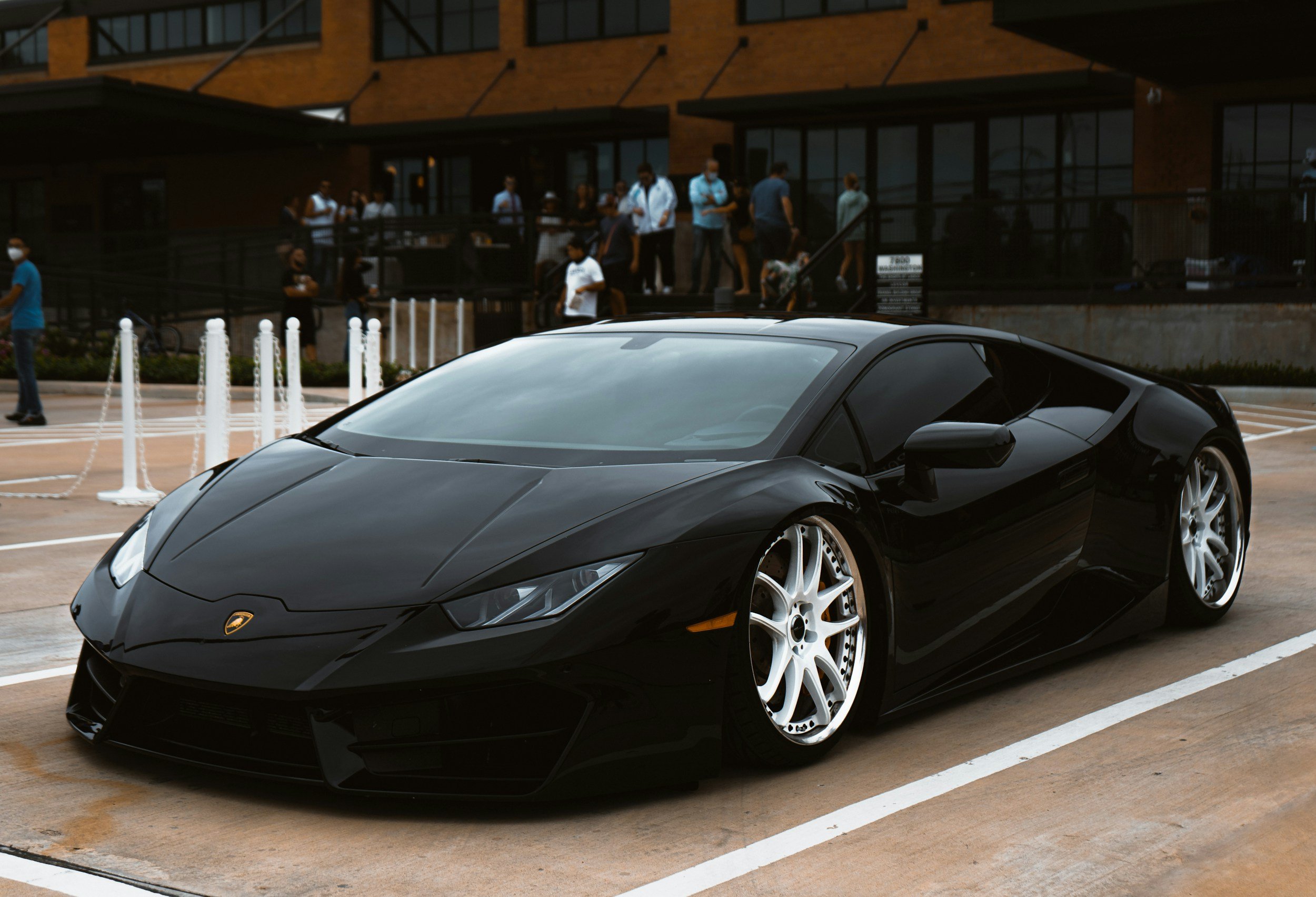 Black Lamborghini sports car parked in a lot with people in the background.