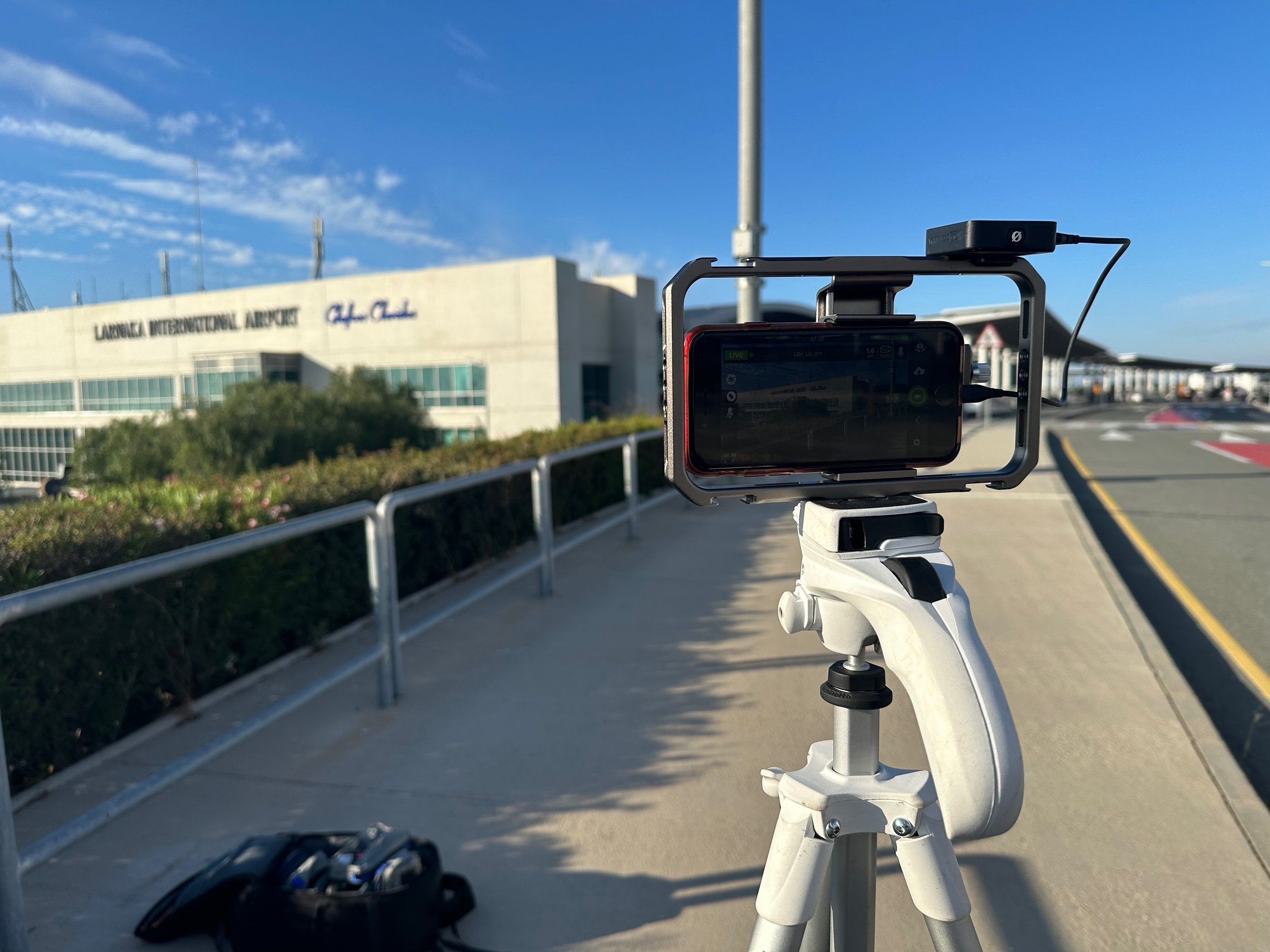 A smartphone mounted on a tripod capturing video or photos outside of Lubbock International Airport on a clear, sunny day.