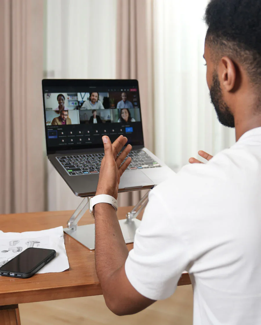 A man participating in a virtual meeting on a laptop, with multiple people visible on the screen.