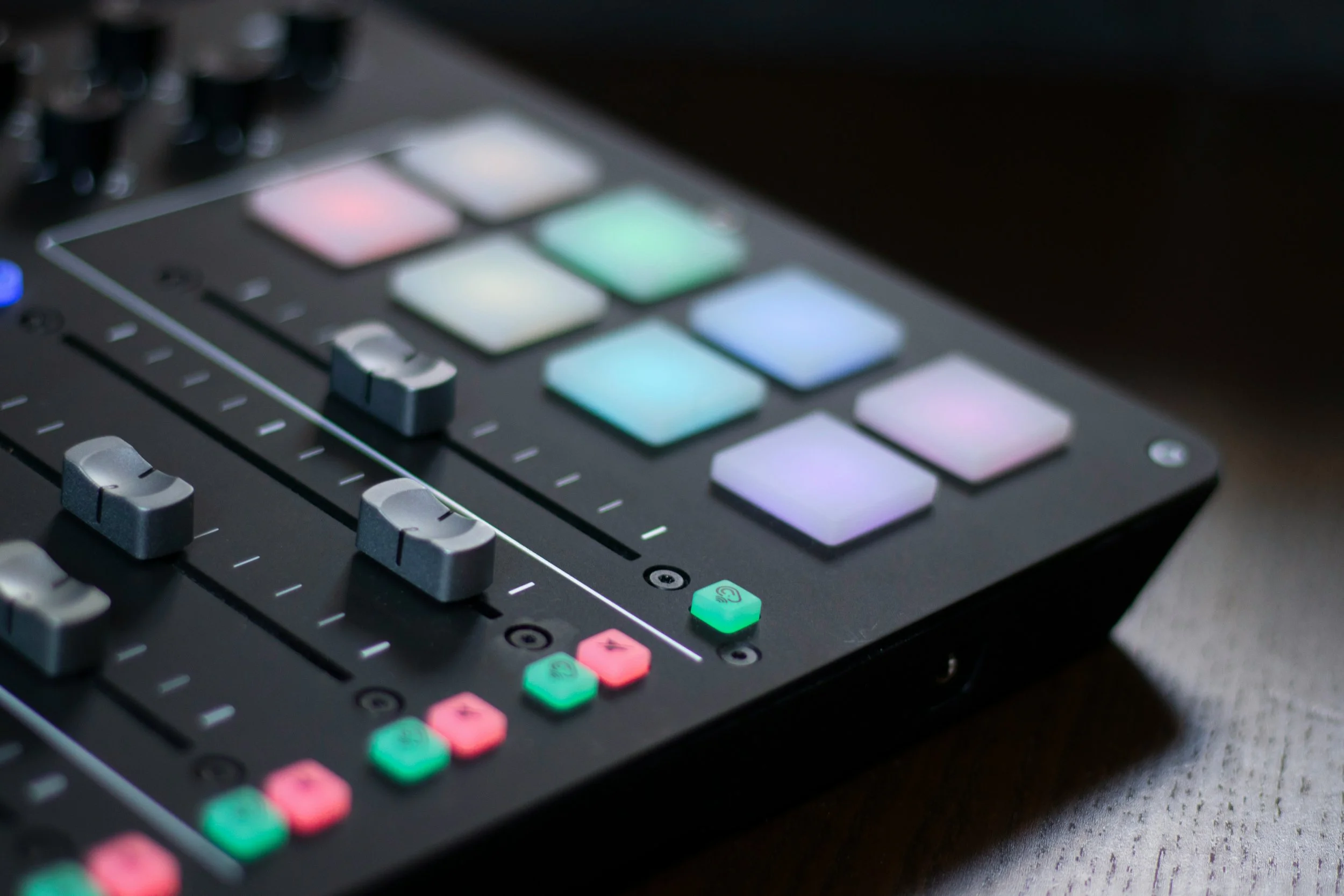 Close-up of a music production controller with illuminated pads and control sliders.