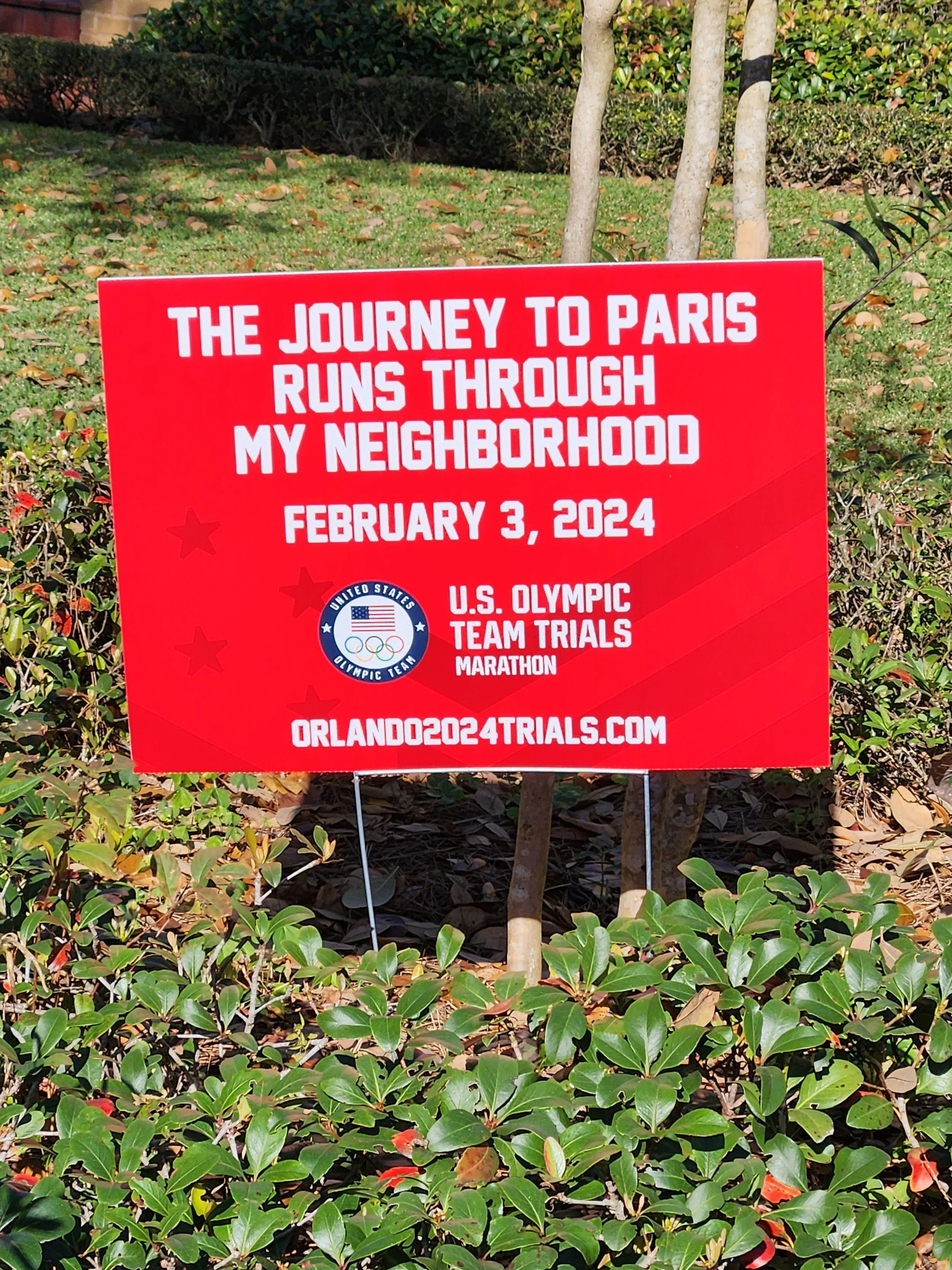 Red sign with white text about the 2024 Olympic Trials, reading: 'The Journey to Paris Runs Through My Neighborhood' scheduled for February 3, 2024.