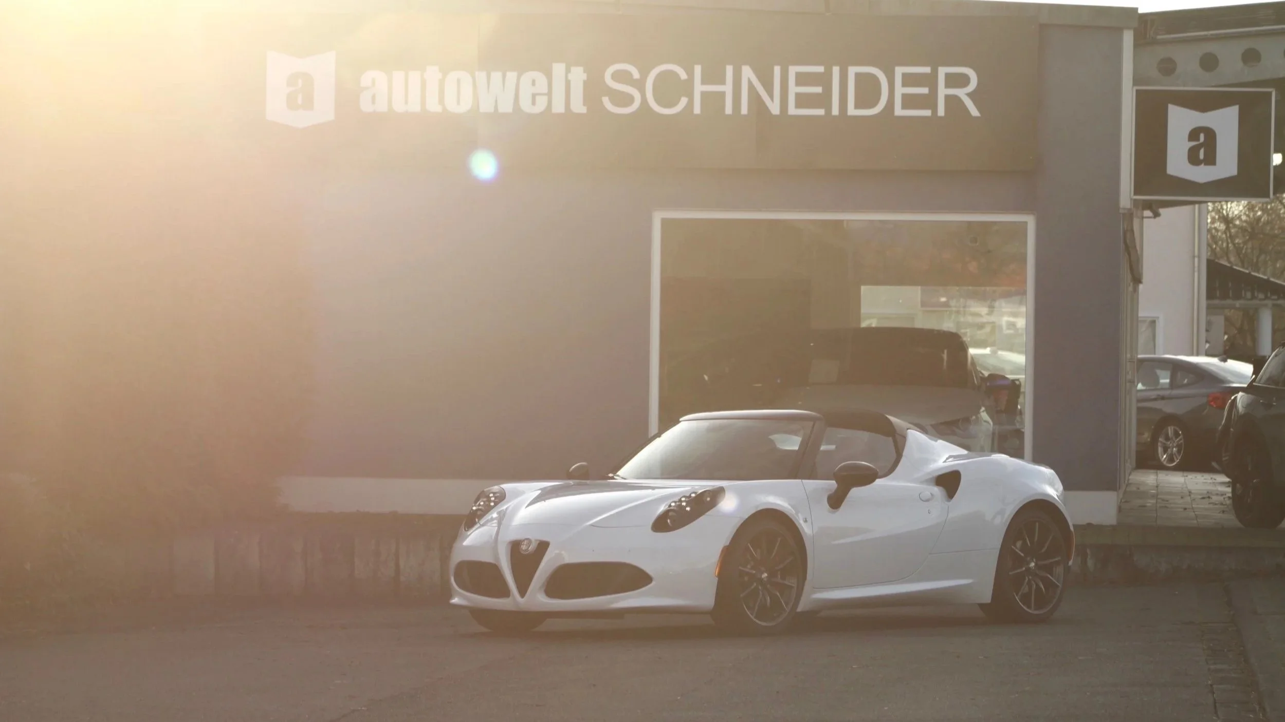 Weißer Sportwagen, Alfa Romeo, vor einem Autohandel 'autowelt SCHNEIDER' mit großen Fenstern und Firmenlogo