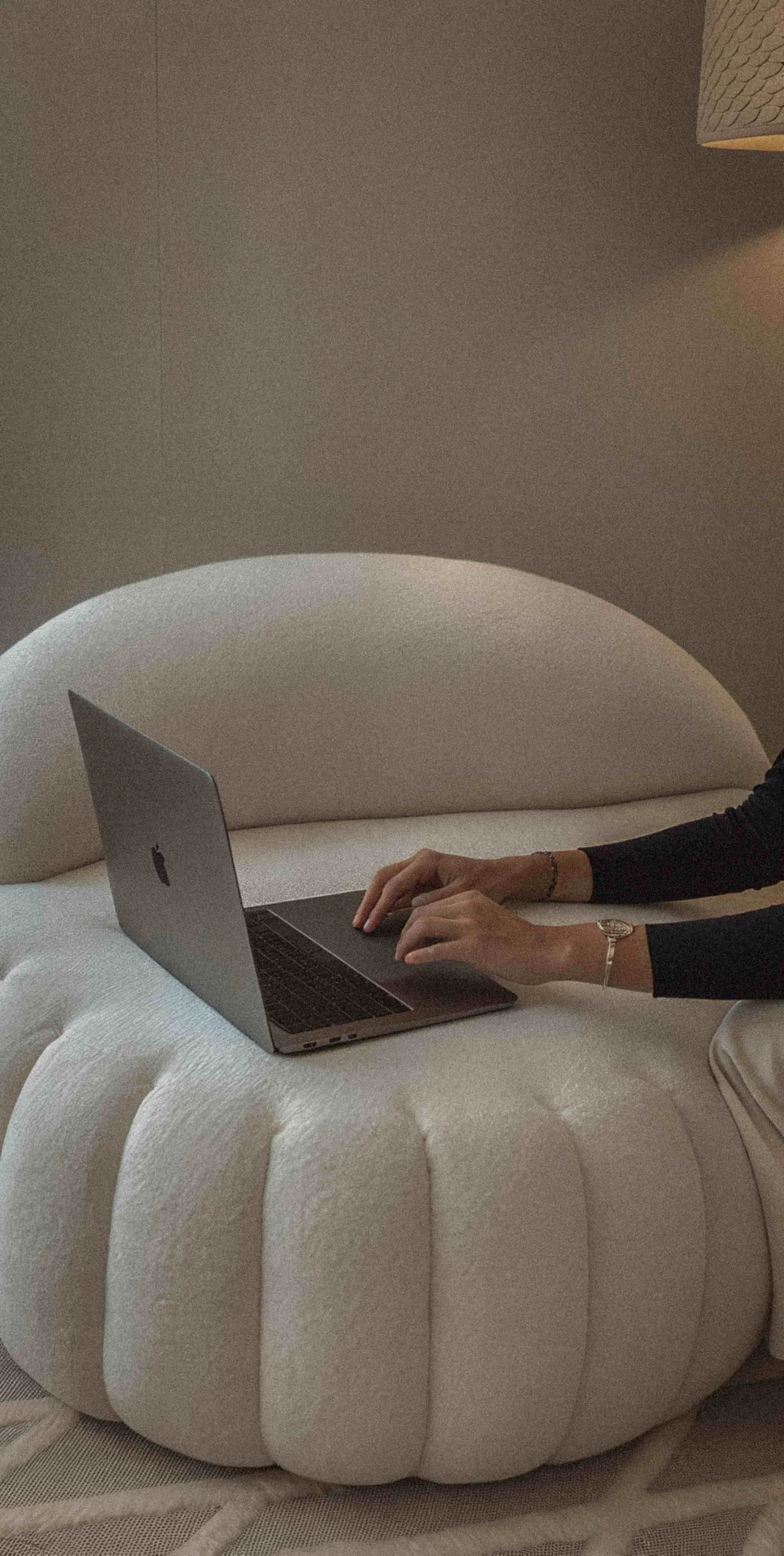 Person working on a MacBook laptop resting on a large, plush, white, scalloped cushion or pillow.