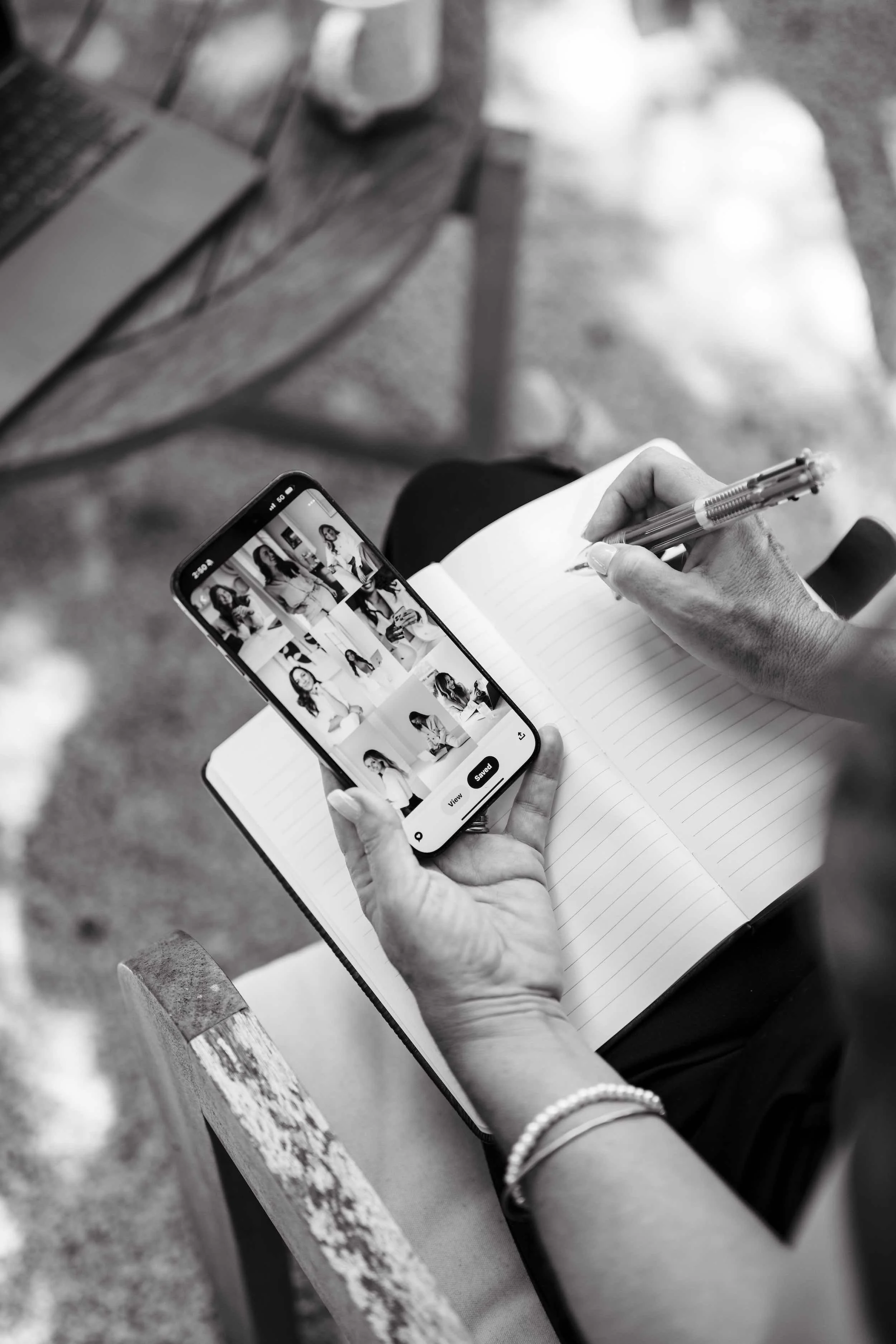 A person taking notes in a notebook while holding a smartphone displaying a collage of black and white portraits of a woman.