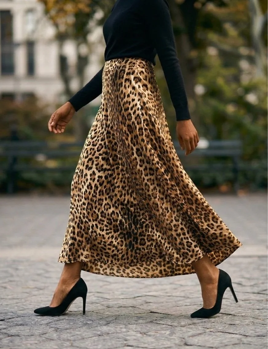 A woman walking on a cobblestone path, wearing a black long-sleeve top, a leopard print maxi skirt, and black high heels.