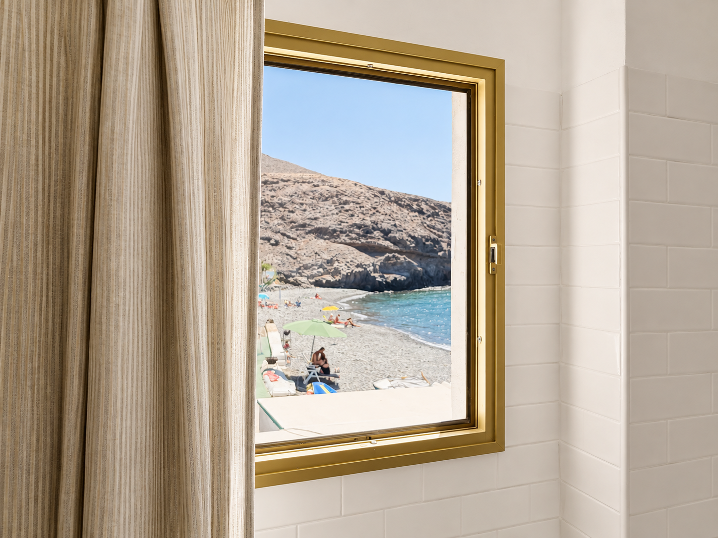 View through an open window showing a rocky coastal landscape with a beach, water, and hills in the distance, partially obstructed by a striped curtain inside the room.