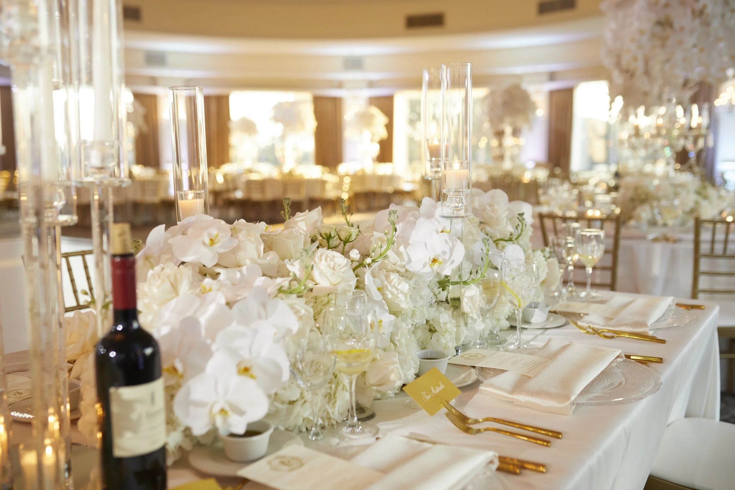 An elegant reception tablescape featuring cascading white florals, candlelight, gold accents, and refined place settings inside the ballroom at Oheka Castle.