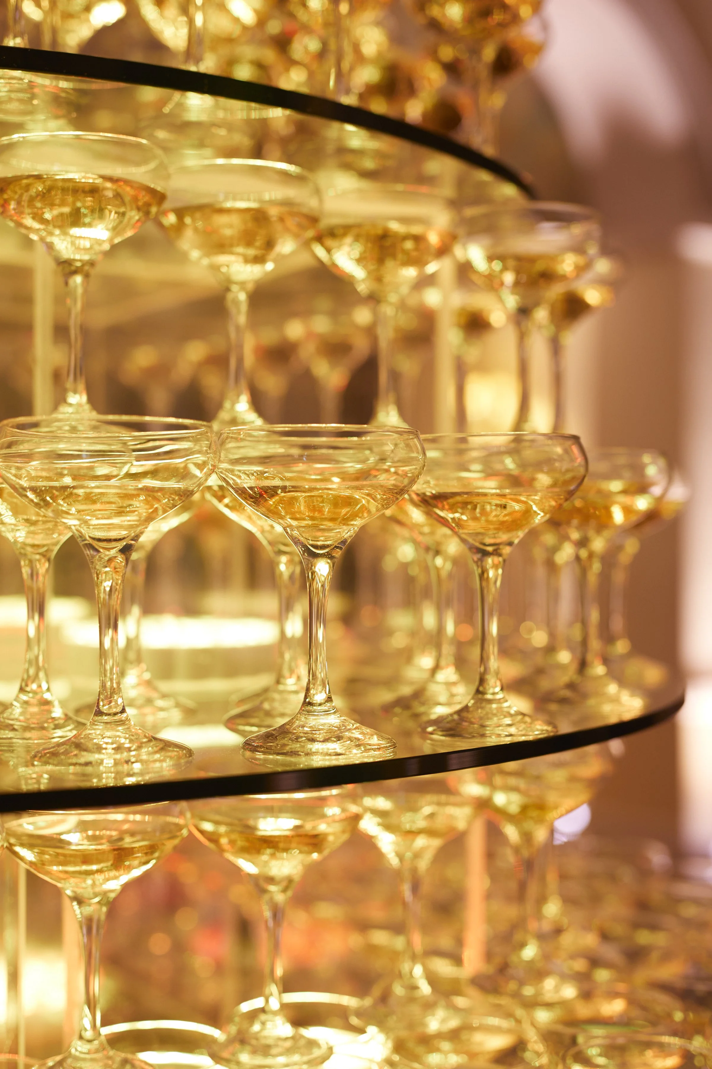 Champagne coupes stacked in glowing golden light during cocktail hour at Samantha and Anthony’s wedding celebration.