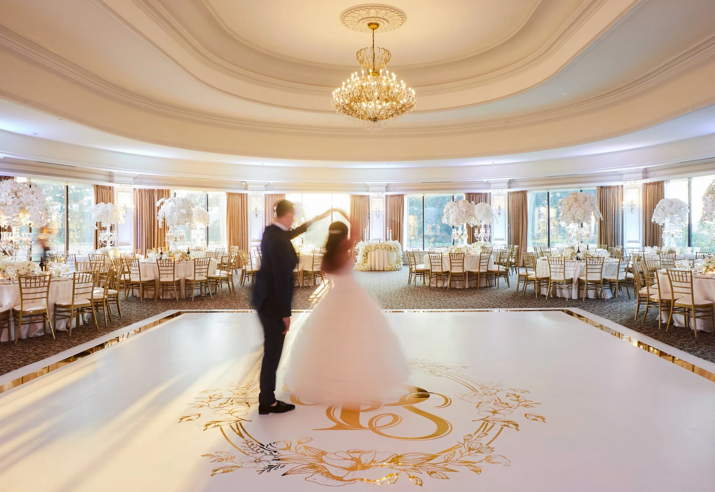 Samantha and Anthony sharing a romantic dance beneath the chandeliers inside the reception ballroom at Oheka Castle surrounded by elegant white floral arrangements and candlelight.